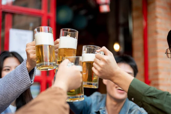 Group of cheerful young Asian friends are cheering, toasting, clinking, or enjoying beer at a restaurant or bar in the city on the weekend together. Lifestyle and friendship concepts. close-up image