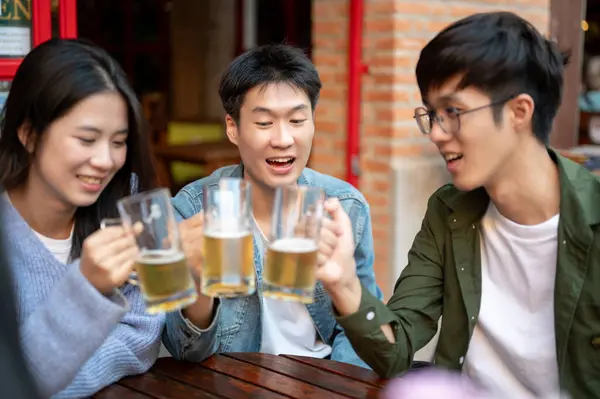 Group of happy young Asian friends are enjoying drinking beers and talking at a bar or restaurant in the city together. hanging out, beer toasting, beer clinking, party, lifestyle