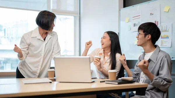 A boss feels satisfied with a project outcome and gives a compliment to her colleagues. Two young office workers are celebrating their project success with their boss in the meeting room.