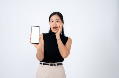 Olumlu ve şaşkın Asyalı bir kadın kameraya akıllı telefon ekranını gösteriyor ve izole edilmiş beyaz bir arkaplana karşı duran çarpıcı yüzünü gösteriyor. Online indirim, beklenmedik haberler