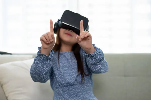 An excited and adorable young Asian girl wearing a VR headset, playing a virtual reality game in the living room. futuristic lifestyle learning, virtual technology