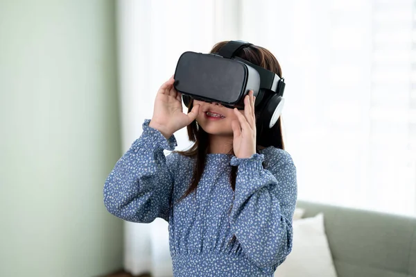 An excited and adorable young Asian girl wearing a VR headset, playing a virtual reality game in the living room. futuristic lifestyle learning, virtual technology