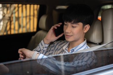 Yakışıklı ve pozitif Asyalı bir işadamı kol saatini kontrol ediyor ve iş yerine giderken telefonla konuşuyor..