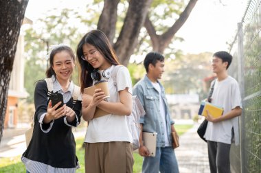 İki genç Asyalı kız öğrenci en iyi arkadaşları akıllı telefondan komik bir video izliyorlar ve kampüslerinde yürürken konuşmaktan keyif alıyorlar. Arkadaşlık ve eğitim kavramları