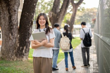 Laptop bilgisayarıyla sıradan kıyafetler giymiş, pozitif, sevimli bir Asyalı kız öğrenci kampüsündeki bir patikada duruyor. Okul konseptine dönelim.