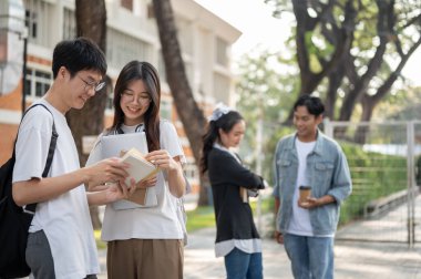 Olumlu Asyalı genç bayan ve erkek üniversite öğrencileri bir kampüs binasının önünde dururken ortak bir projeden bahsediyorlar. Eğitim ve arkadaşlık kavramları