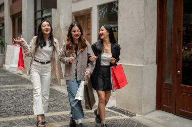 Bir grup güzel ve neşeli Asyalı genç kız alışveriş torbalarıyla yürüyor, gülüyorlar, hafta sonları alışveriş caddesinde birlikte alışveriş yapıyorlar. Moda ve yaşam tarzı kavramları