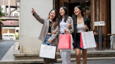 Güzel Asyalı genç kız arkadaşlar alışveriş çantalarını alıp şehirde alışveriş günlerinin tadını çıkarıyorlar. Yurt dışına seyahat, turizm, tüketim, moda ve yaşam tarzı