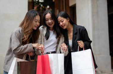 Bir grup neşeli ve eğlenceli Asyalı genç kız arkadaş birlikte alışveriş günlerinin tadını çıkarıyorlar, satın aldıkları şeyleri çantalarında arıyorlar. Tüketim, alışveriş, moda, şehir hayatı