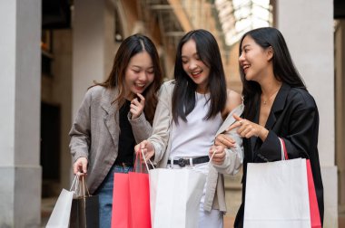 Bir grup neşeli ve eğlenceli Asyalı genç kız arkadaş birlikte alışveriş günlerinin tadını çıkarıyorlar, satın aldıkları şeyleri çantalarında arıyorlar. Tüketim, alışveriş, moda, şehir hayatı