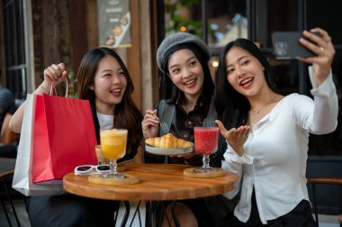 Bir grup çekici Asyalı bayan arkadaş bir restoran ya da kafede takılırken akıllı telefonlarıyla selfie çekiyorlar. Şehir hayatı, seyahat, yaşam tarzı.