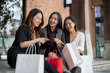 Genç mutlu Asyalı üç bayan arkadaş hafta sonu birlikte alışveriş yapmak için şehrin merdivenlerinde oturuyorlar. Yaşam tarzı ve moda kavramları
