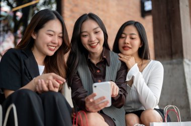 Bir grup mutlu ve güzel Asyalı kız şehirde alışveriş yaptıktan sonra merdivenlerde dinlenirken sohbet ediyorlar. Yaşam tarzı, şehir hayatı, moda.