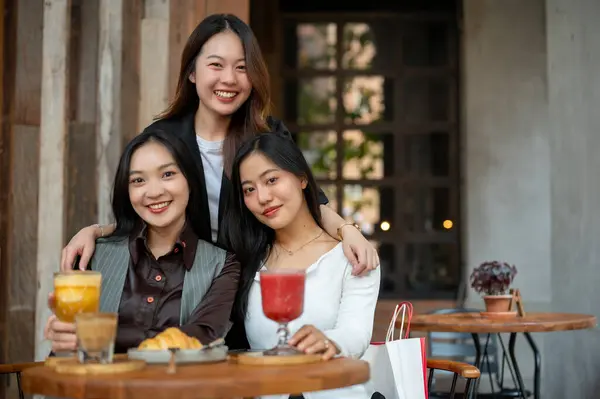 Three attractive young Asian women are sitting at a table in a restaurant together, hanging out on the weekend. City life and friendship concepts