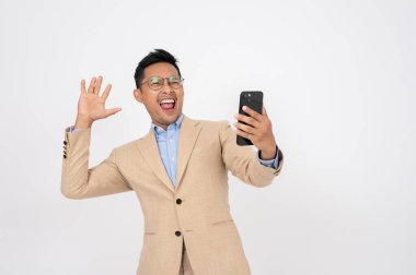 Şaşırmış ve heyecanlı bir Asyalı işadamı, izole edilmiş beyaz bir arka planda dururken şaşırtıcı bir yüzle telefon ekranına bakıyor. Sıcak anlaşma, beklenmedik haberler, vay canına, inanılmaz.
