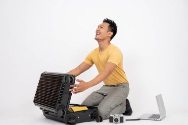 Mutlu, yakışıklı Asyalı bir adam tatil gezisi için heyecanlı, bavullarını topluyor, izole edilmiş beyaz bir stüdyoda oturuyor. Tatil, turist, seyahat