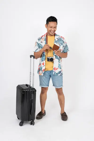 stock image A cheerful, excited Asian man in summer clothes is standing on an isolated white studio background with his luggage. summer vacation, holiday trip, traveling