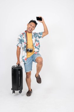 Yaz kıyafetleri içinde neşeli bir Asyalı yaz tatili için heyecanlı ve plajda bagajlarıyla izole edilmiş beyaz bir stüdyoda duruyor. yaz tatili konsepti