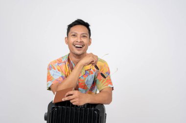 Yaz kıyafetleri içinde mutlu bir Asyalı pasaport ve bavuluyla izole edilmiş beyaz bir stüdyoda poz veriyor. Yaz tatili, sahil gezisi, tatil