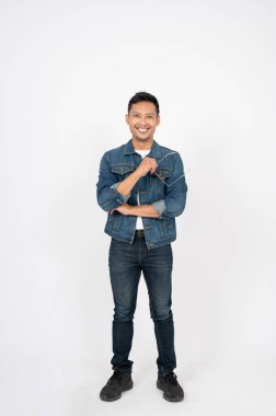 Kot ceketli yakışıklı, pozitif Asyalı bir adamın portresi kameraya gülümsüyor ve izole edilmiş beyaz bir arka planda dururken güneş gözlüğünü tutuyor..