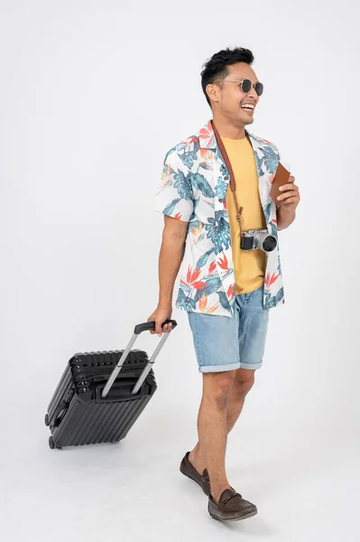 Stock image A positive, handsome Asian man in summer clothes walking with his luggage and passport on an isolated white studio background. travel, holiday, summer trip