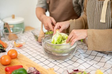 Bir çiftin yakın plan görüntüsü, karı koca, mutfakta birlikte salata kasesi yapıyorlar, kahvaltıları için sağlıklı yemek hazırlıyorlar..