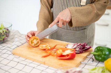 Önlüklü bir kadının yakın plan görüntüsü domatesi doğruyor, mutfakta yemeği için taze malzemeler hazırlıyor. Ev yemeği, sağlıklı yemek, diyet yemek.