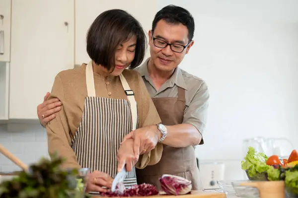 A caring Asian husband teaches and helps his wife chop vegetables, prepare ingredients, and cook in the kitchen together. husband and wife, couple, domestic life