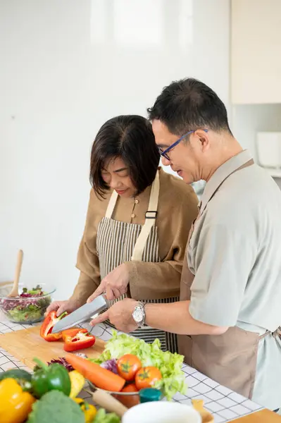 A happy, lovely Asian wife is chopping a sweet pepper while her husband is helping her, enjoy cooking in the kitchen together. home cooking, domestic life, happy quality time, people and food