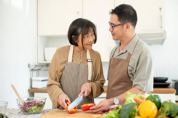 A happy, lovely Asian wife is chopping a sweet pepper while her husband is helping her, enjoy cooking in the kitchen together. home cooking, domestic life, happy quality time, people and food