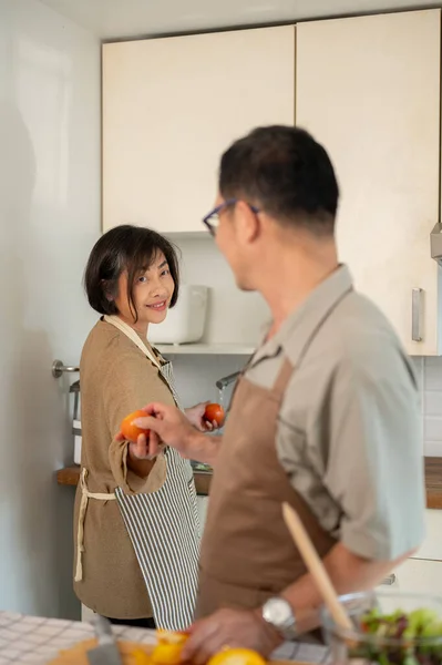 A lovely and happy Asian wife is cooking with her husband in the kitchen, spending a happy quality time together at home. Home cooking, domestic life, adult couple