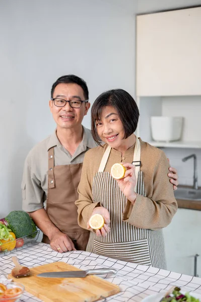 A lovely and happy adult Asian couple is in the kitchen, wearing apron, preparing to cook their dinner together. wife and husband, domestic life, home cooking