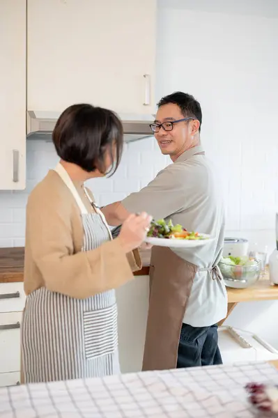 A lovely Asian couple enjoys eating food after cooking it together in the kitchen, spending a happy quality time at home on the weekend. Adult couples, domestic life, healthy lifestyle