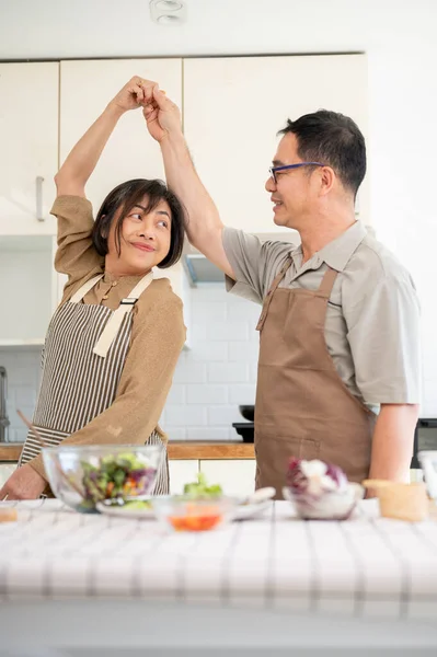 A lovely, romantic Asian couple dances in the kitchen and enjoys cooking together. family bonding, wife and husband, domestic life