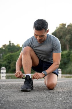 Spor giyimli güçlü, formda bir Asyalı ayakkabı bağcıklarını bağlıyor ve parkta egzersiz yapmadan önce hazırlanıyor. hobi ve sağlıklı yaşam tarzı kavramları