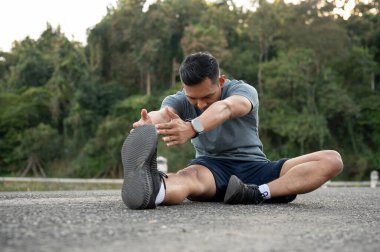 Spor giyimli mutlu ve güçlü bir Asyalı adam spor yapmadan önce ya da egzersizden sonra ısınmak için vücudunu dışarıda geriyor. Koşucu, koşucu, atlet