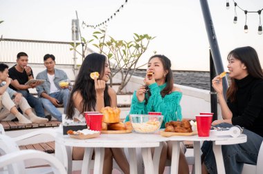 Bir grup neşeli Asyalı genç bayan arkadaş çatıdaki bir restoranda parti yaparken gülüyor, eğleniyor ve abur cubur yiyor. Kızlar gecesi, kutlama, şehir hayatı.