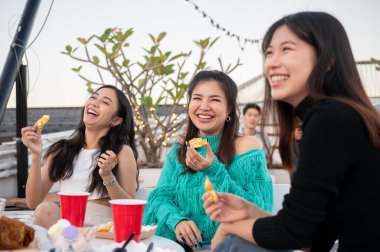 Bir grup neşeli Asyalı genç bayan arkadaş çatıdaki bir restoranda parti yaparken gülüyor, eğleniyor ve abur cubur yiyor. Kızlar gecesi, kutlama, şehir hayatı.