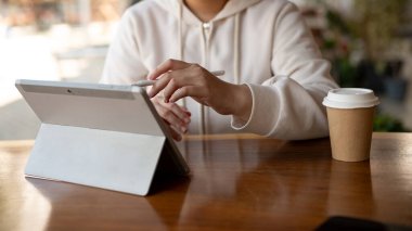 Bir bayan üniversite öğrencisi ya da bir serbest çalışan bir kafede otururken dijital tabletini kullanıyor. Kesilmiş görüntü, kablosuz teknoloji ve insanların kavramları