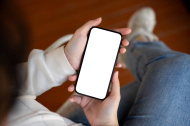 Bir kadın evde oturuyor ve akıllı telefonunu kullanıyor. Bir kadının elindeki beyaz ekran cep telefonunun yakın plan görüntüsü. İnsanlar ve teknoloji kavramları