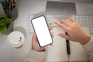 Bir kadının en iyi görüntüsü, ofis masasında akıllı telefonunu kullanmasıdır. Grafik reklamlarınızı göstermek için beyaz ekran akıllı telefon modeli. İnsanlar ve teknoloji kavramları