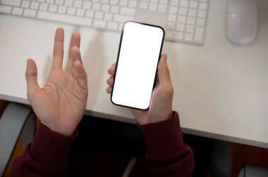 Memnuniyetsiz bir ofis çalışanının üst görüntüsü ofis masasındaki akıllı telefonundaki mesajları kontrol ediyor. İnsanlar ve teknoloji kavramları