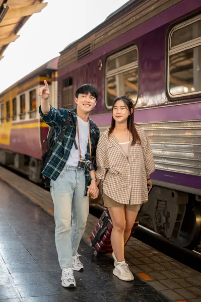 Young happy Asian couple travelers are commuting by train together, walking on a platform at a railway station, and catching the train. People and transportation concepts