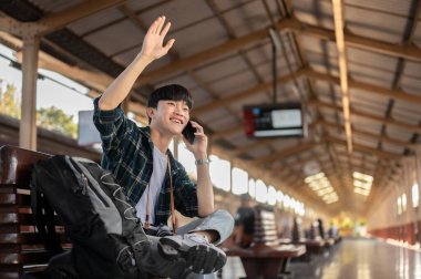 Yakışıklı bir Asyalı genç adam, bir tren istasyonunda onu beklerken arkadaşıyla telefonda konuşurken elini sallıyor, platformdaki bir bankta oturuyor. Halk ve toplu taşıma kavramları