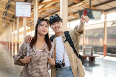 Güzel ve mutlu bir Asyalı çift tren istasyonunda trenlerini beklerken trenle birlikte seyahat ediyorlar. Yaşam tarzı, yaz tatili, toplu taşıma, banliyö