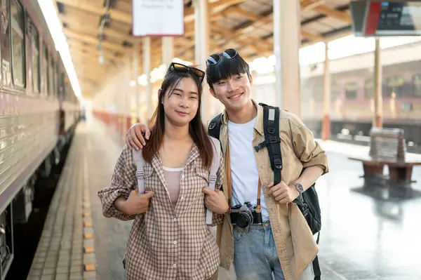 A lovely and happy young Asian couple of travelers are traveling by train together, waiting for their train at a railway station. Lifestyle, summer vacation, public transportation, commuter