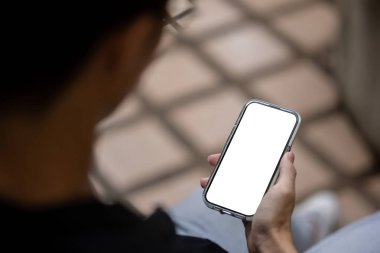 Açık havada otururken akıllı telefonunu kullanan bir adamın yakın plan görüntüsü. Beyaz ekran akıllı telefon modeli bir adamın elindedir. İnsanlar ve teknoloji kavramları