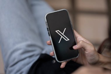 Chiang Mai, Tayland - 16 Ocak 2024: Açık havada otururken iPhone 'unda X uygulamasını kullanan bir adam. iPhone ekranında X veya yeni Twitter logosu. yakın plan resim