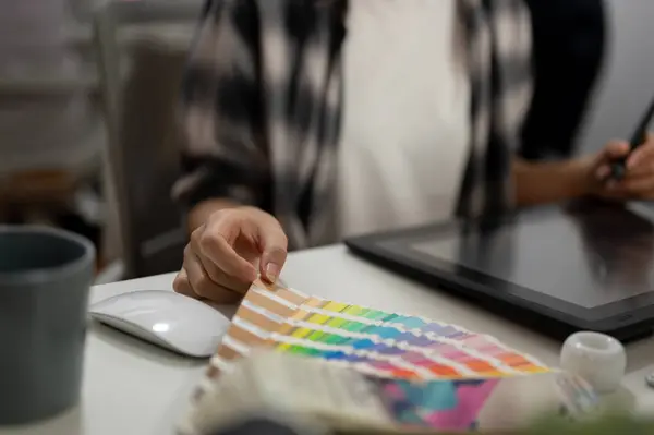 Cropped image of a professional female graphic designer illustrator artist working in the office, color swatch samples on the table.