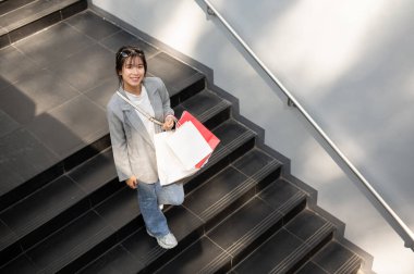 Güzel, modaya uygun Asyalı bir kadın alışveriş torbalarıyla merdivenlerden iniyor ve hafta sonları şehirde alışveriş gününün tadını çıkarıyor. şehir hayatı konsepti